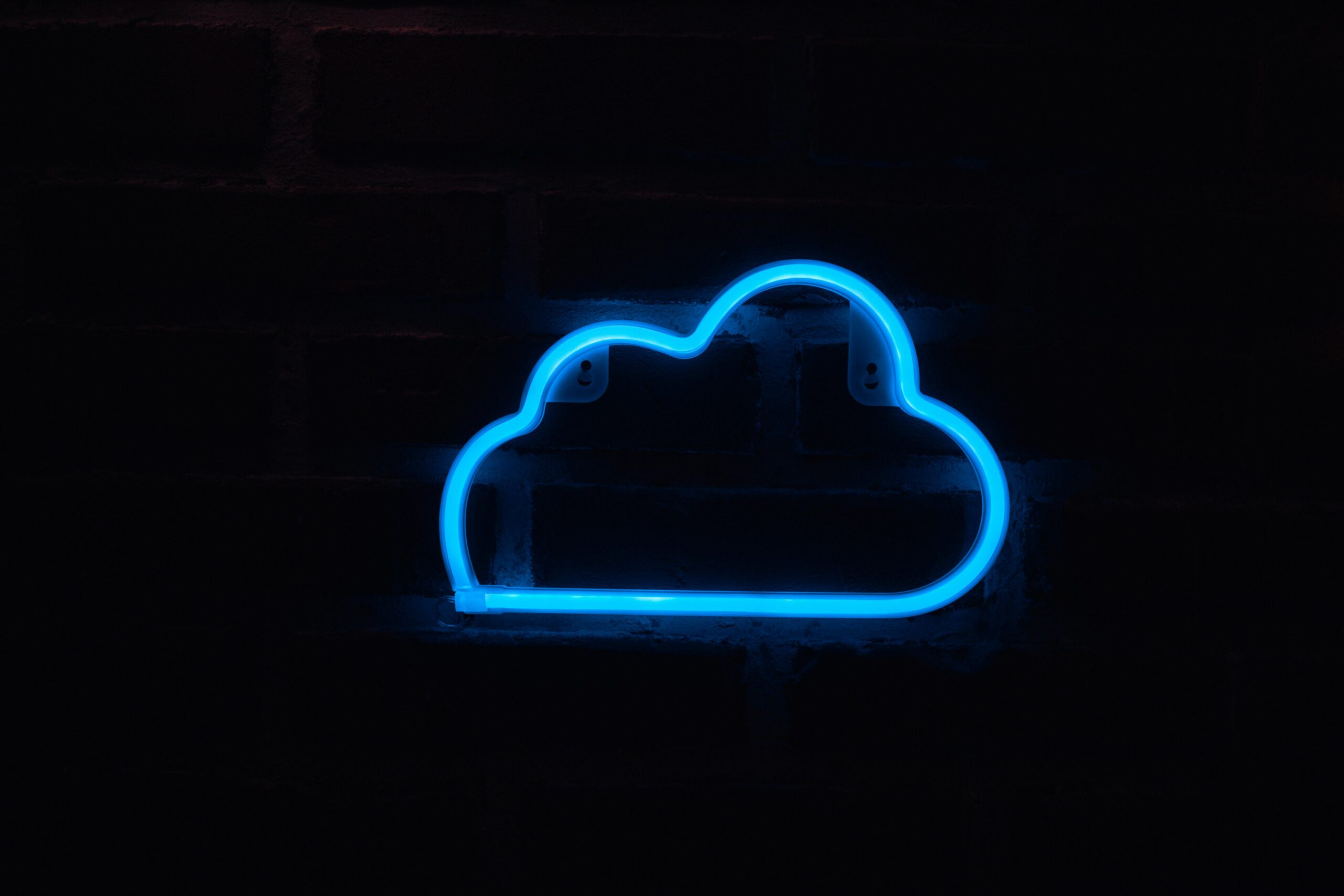 A bright blue neon cloud sign glowing against a dark brick wall background.